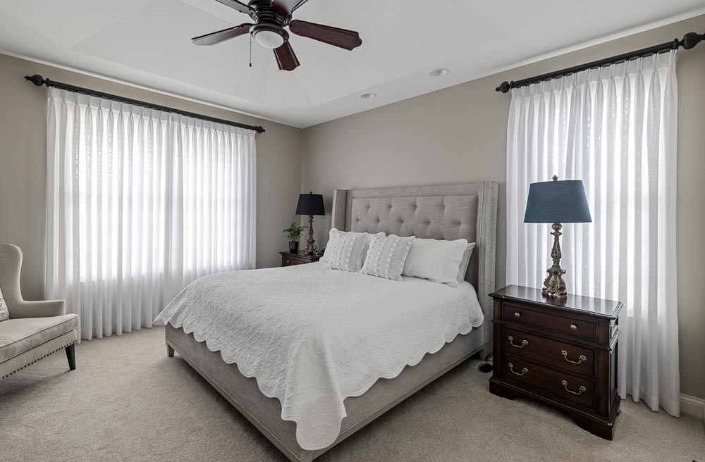 A beautiful bedroom with customized pinch pleat drapery panels by Sunshine Drapery