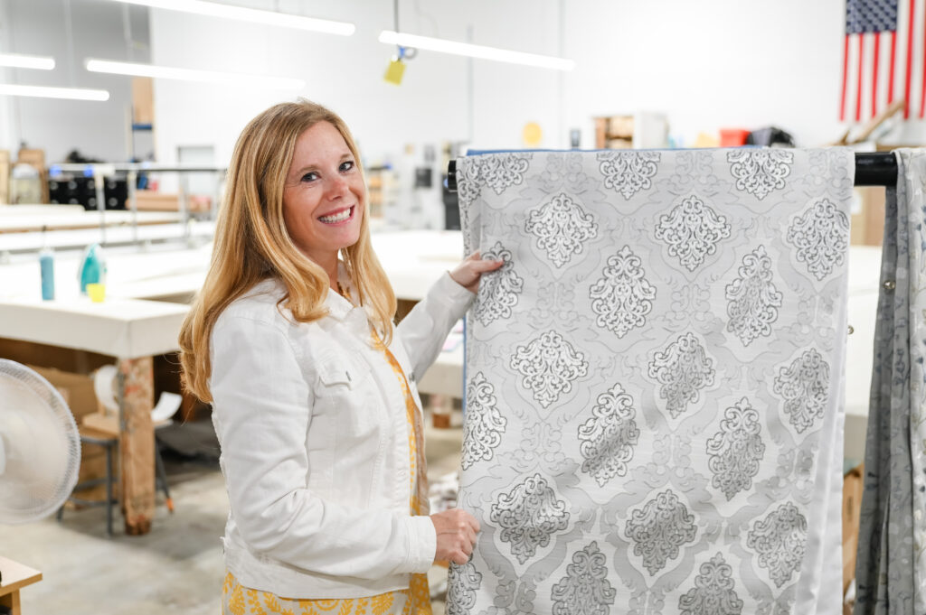 Taira Price, Co-Owner of Sunshine Draperies, Blinds, Shades, and Shutters displaying a beautiful piece of drapery fabric.