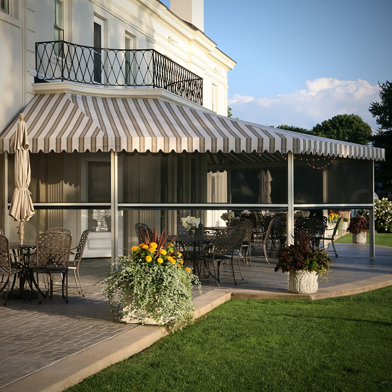Elegant backyard patio featuring a striped retractable awning, outdoor dining area, and motorized shade screens for sun protection.